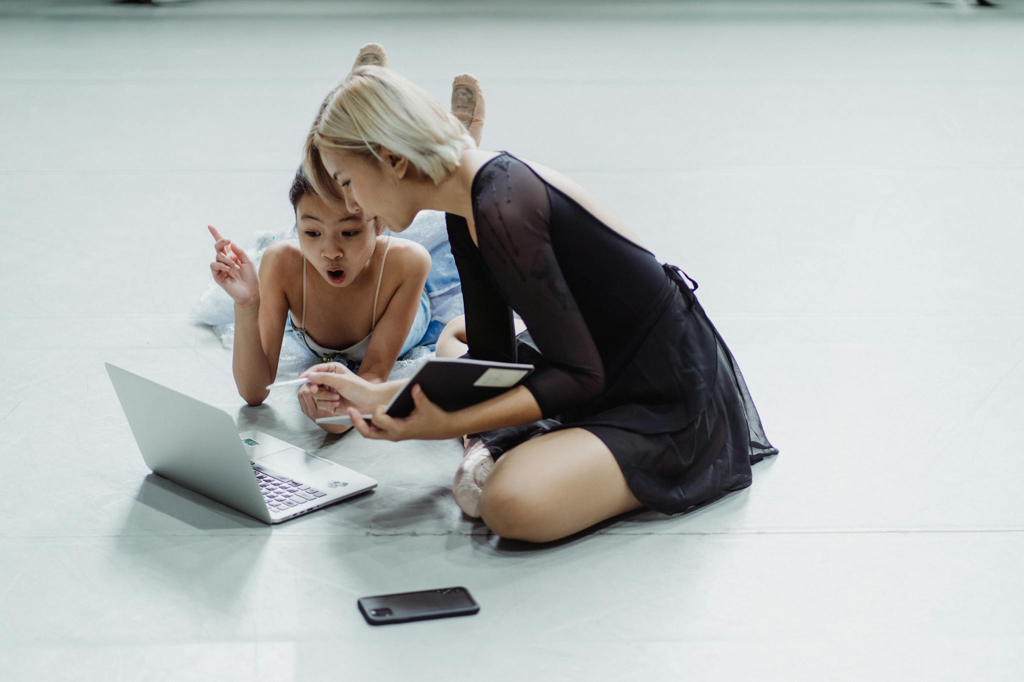 Two female ballet dancers engaged in online learning, showing surprise and interest.